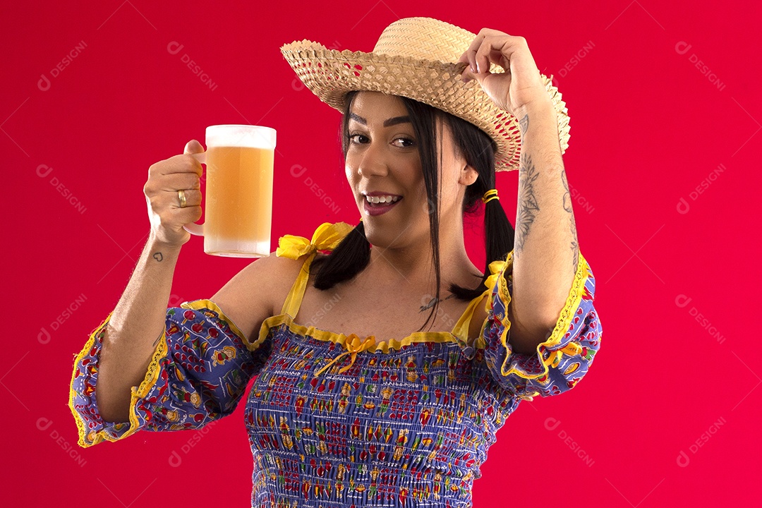 Jovem com chapéu e roupa junina tomando uma caneca de cerveja