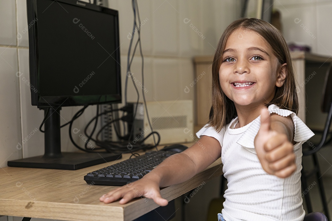 Garotinha feliz sentada em uma mesa com computador
