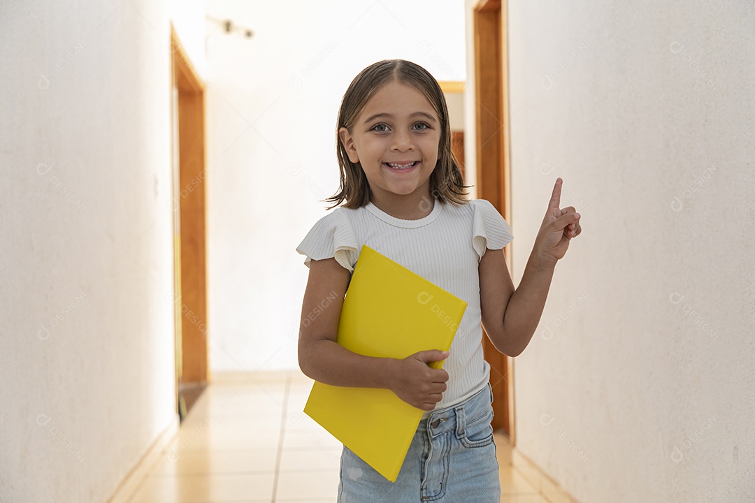Garotinha linda com caderno na mão apontando para cima