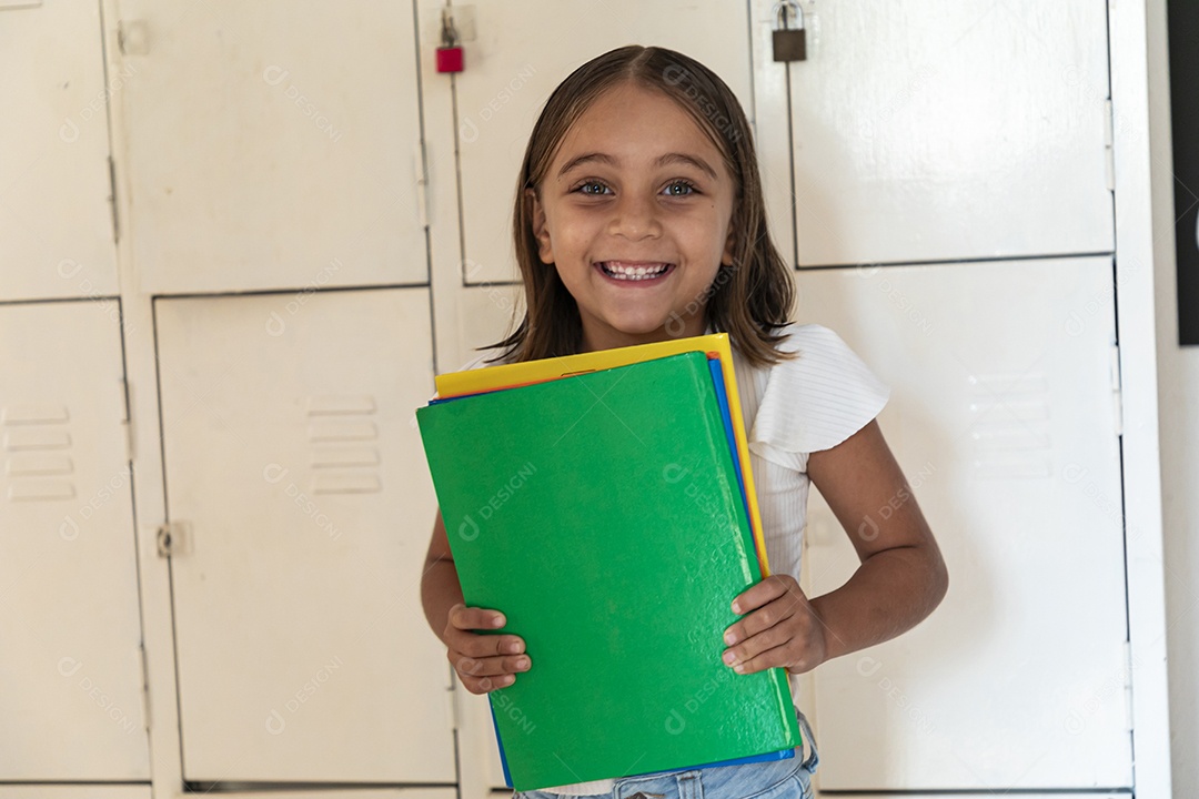 Menininha linda com muitos livros nas mãos em uma escola