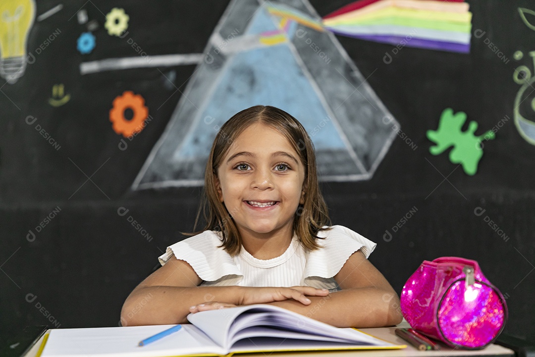 Linda menina com caderno aberto feliz na sua sala de aula