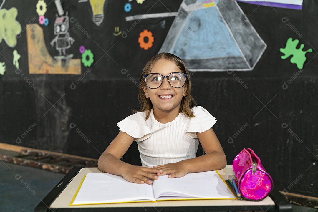 Uma garotinha feliz sentada numa carteira de escola estudando