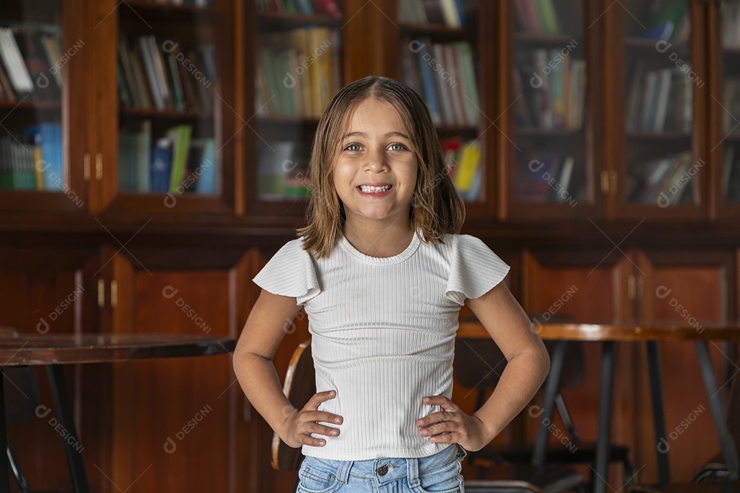 Linda menina com mãos na cintura e sorrindo em uma livraria