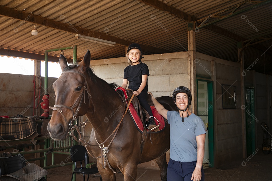 Linda garotinha montada a um cavalo para aula de hipismo