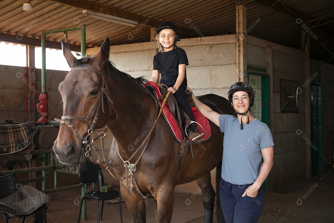 Uma garotinha montada a um cavalo e sua treinadora ao lado