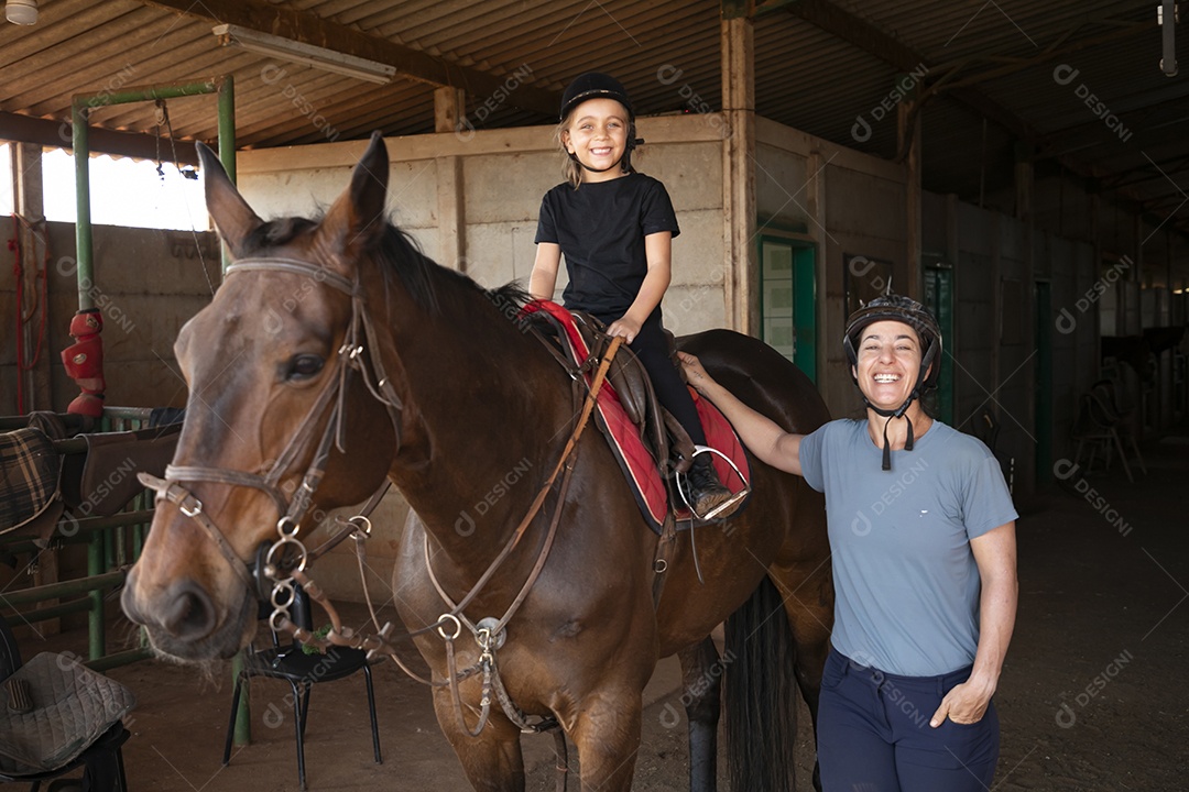 Uma garotinha montada a um cavalo e sua treinadora ao lado