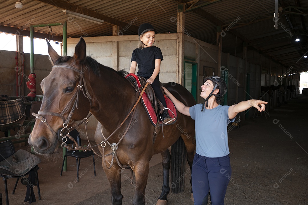 Uma garotinha montada e sua treinadora ao lado