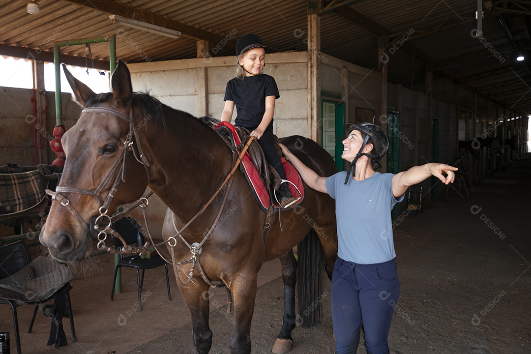 Uma garotinha montada e sua treinadora ao lado