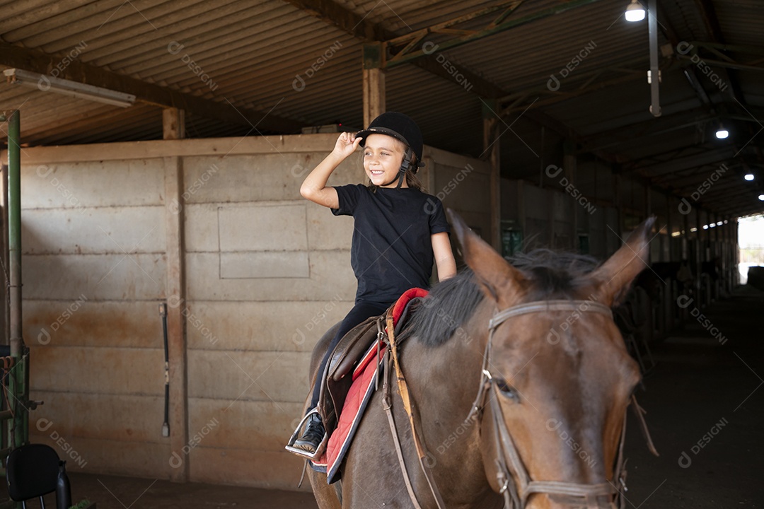 Linda garotinha montada a um cavalo para aula de hipismo