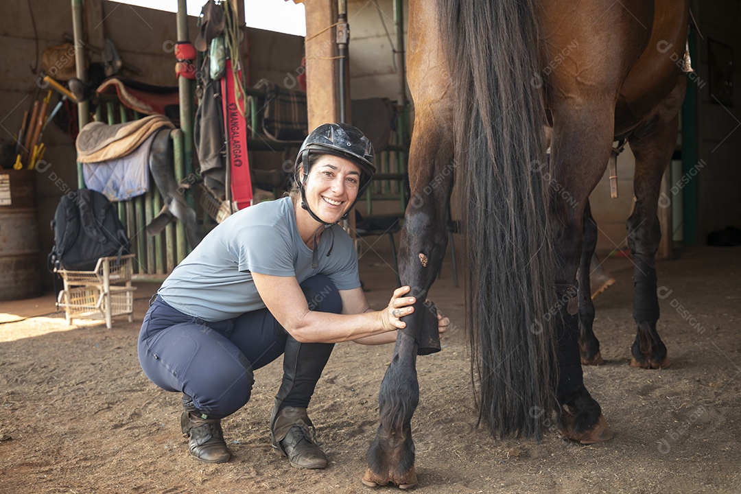 Mulher cuidando do seu cavalo colocando baixa na perna