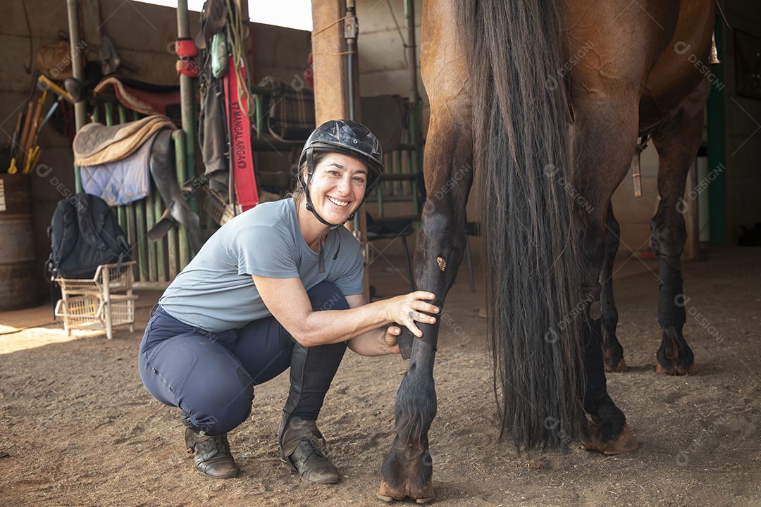 Mulher cuidando do seu cavalo colocando baixa na perna