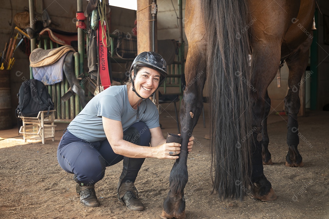 Mulher cuidando do seu cavalo colocando baixa na perna
