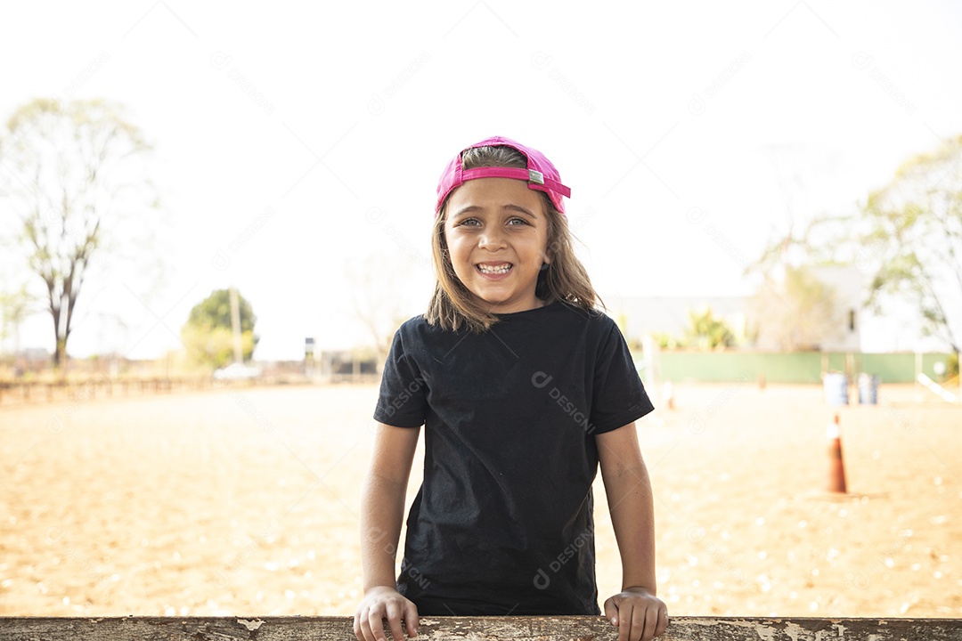Linda garotinha de boné sorrindo se divertindo no treino de hipismo