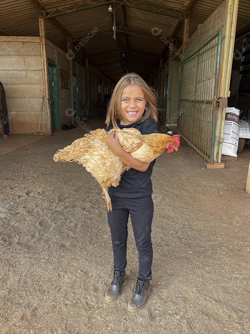 Uma garotinha feliz com sua galinha nas mãos