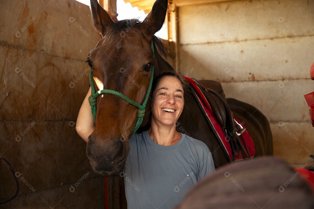 Mulher feliz abraçada com seu cavalo em uma baia