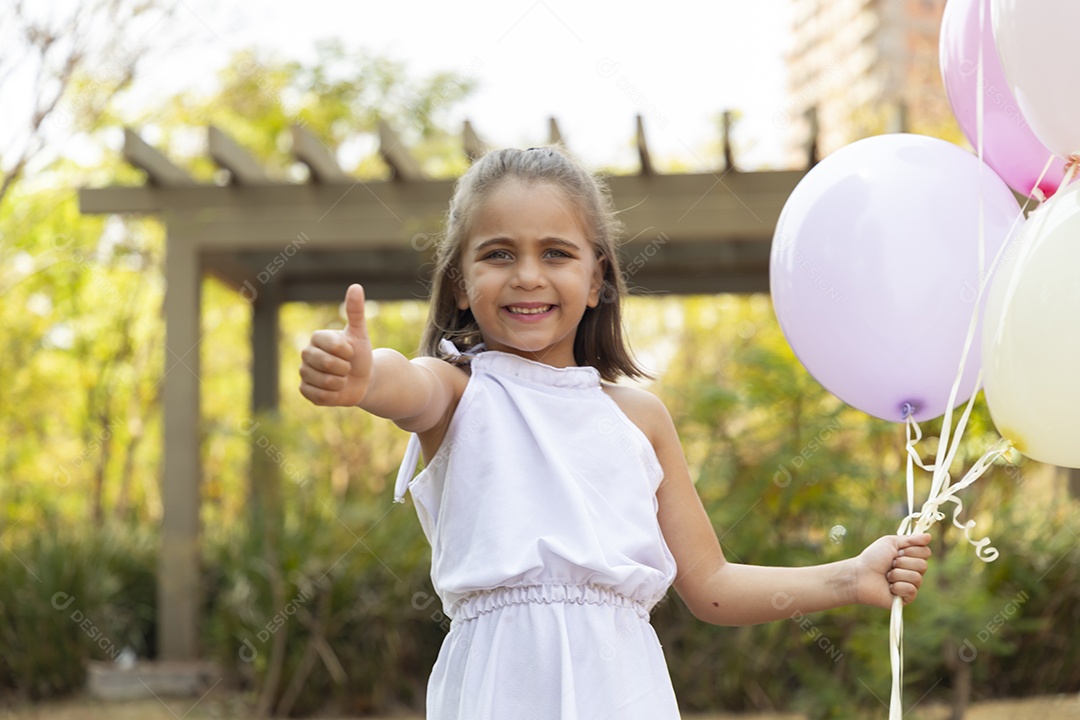 Linda garotinha com balões na mão e gesto de legal