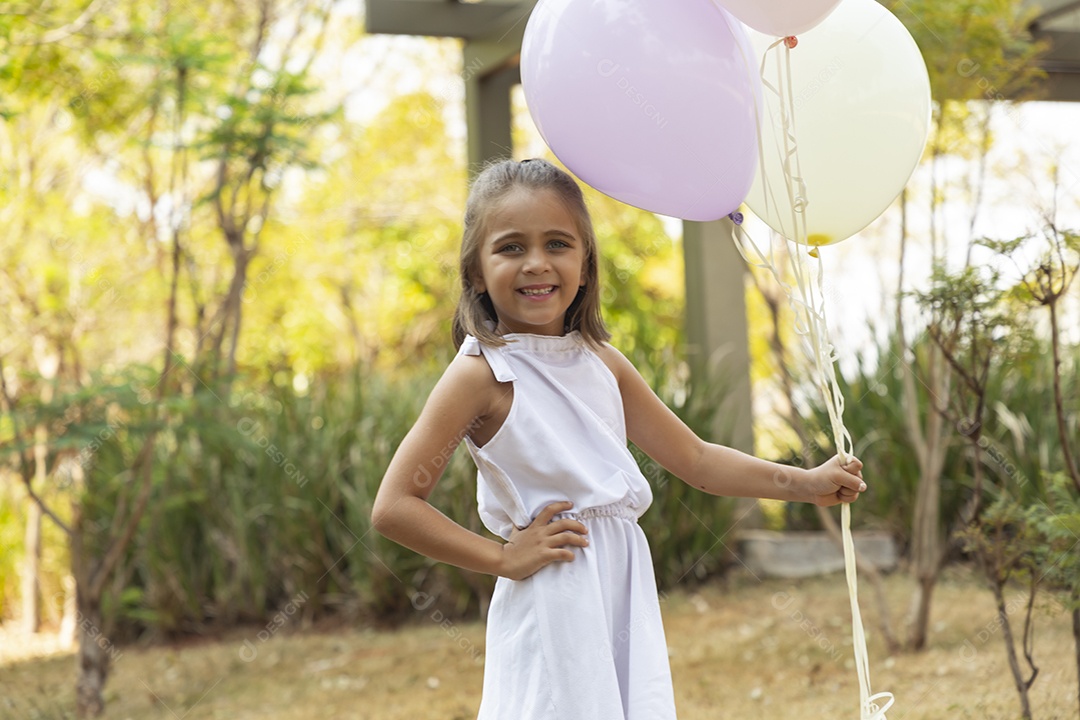 Linda garotinha com mãos na cintura e segurando balões para foto