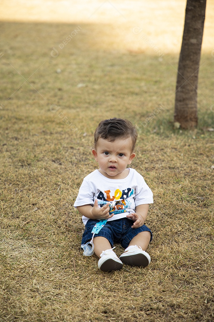 Um garotinho lindo sentado na grama para fotos
