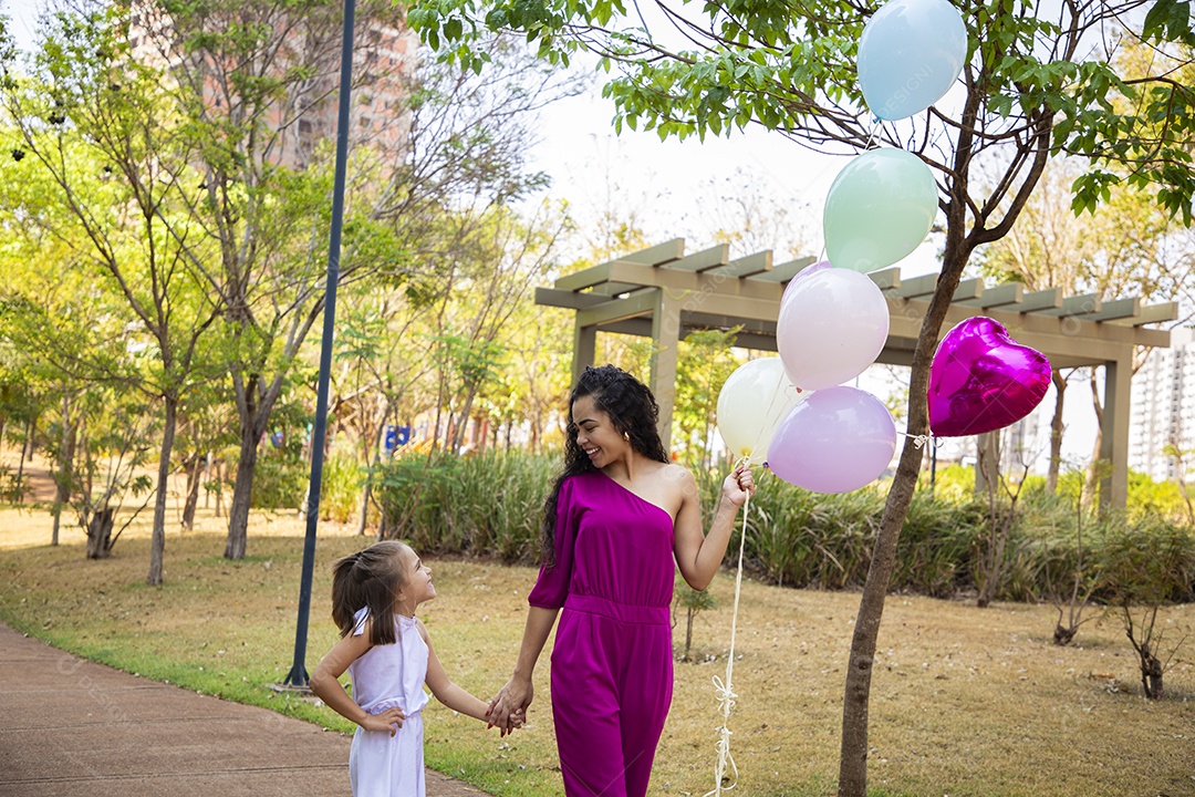 Mãe e filha de mãos dada com balões para foto