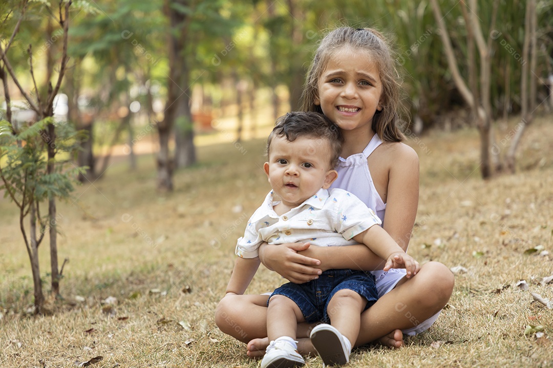 Menininha linda segurando seu irmãozinho no parque