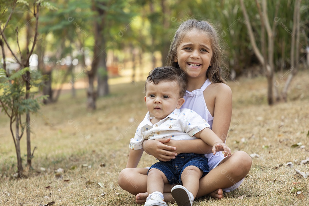 Linda menininha sentada com seu irmão no colo