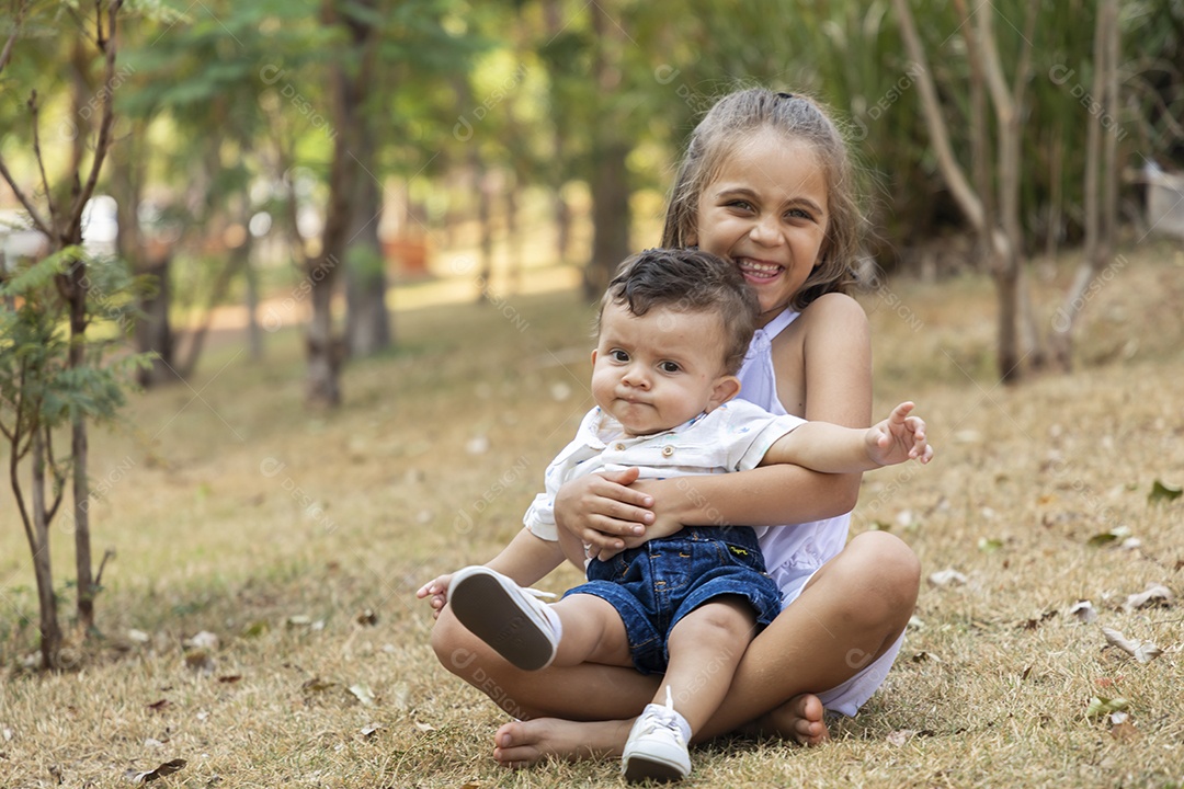 Uma menininha linda segurando seu irmãozinho no parque