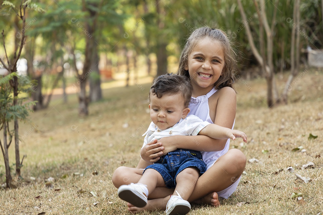 Menininha linda segurando seu irmãozinho no parque