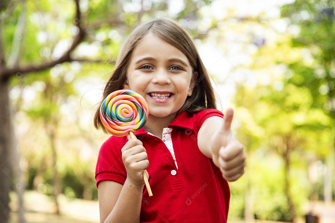 Linda menina com pirulito na mão e gesto de legal