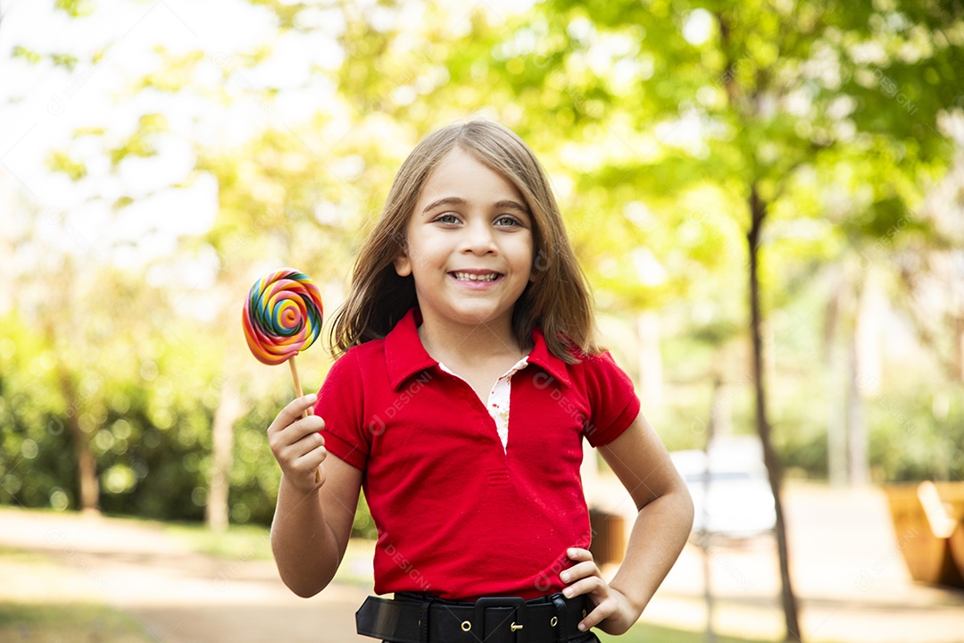 Linda garotinha em um parque feliz com um pirulito nas mãos