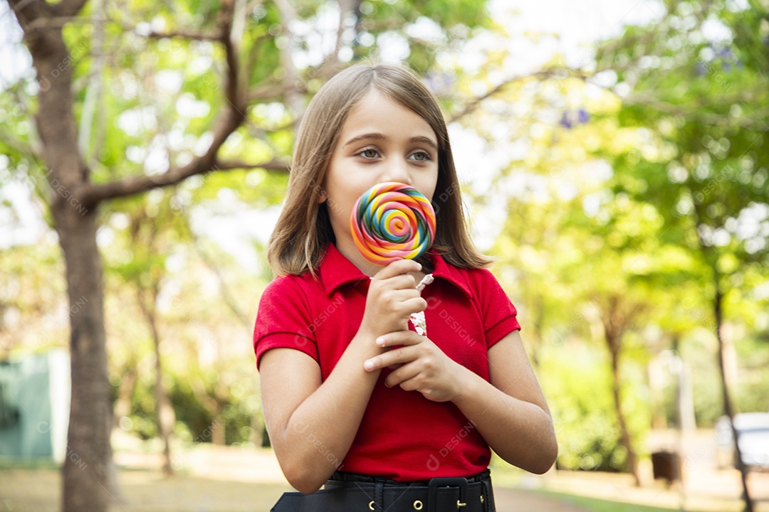 Uma linda menininha no parque chupando um pirulito