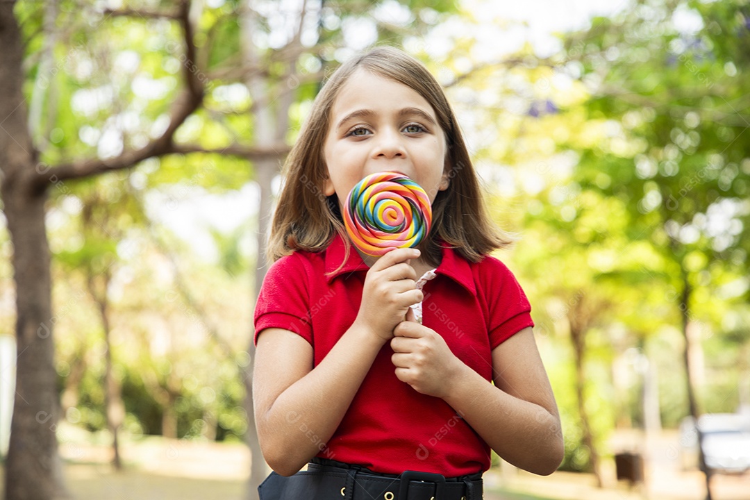 Uma linda menininha no parque chupando um pirulito