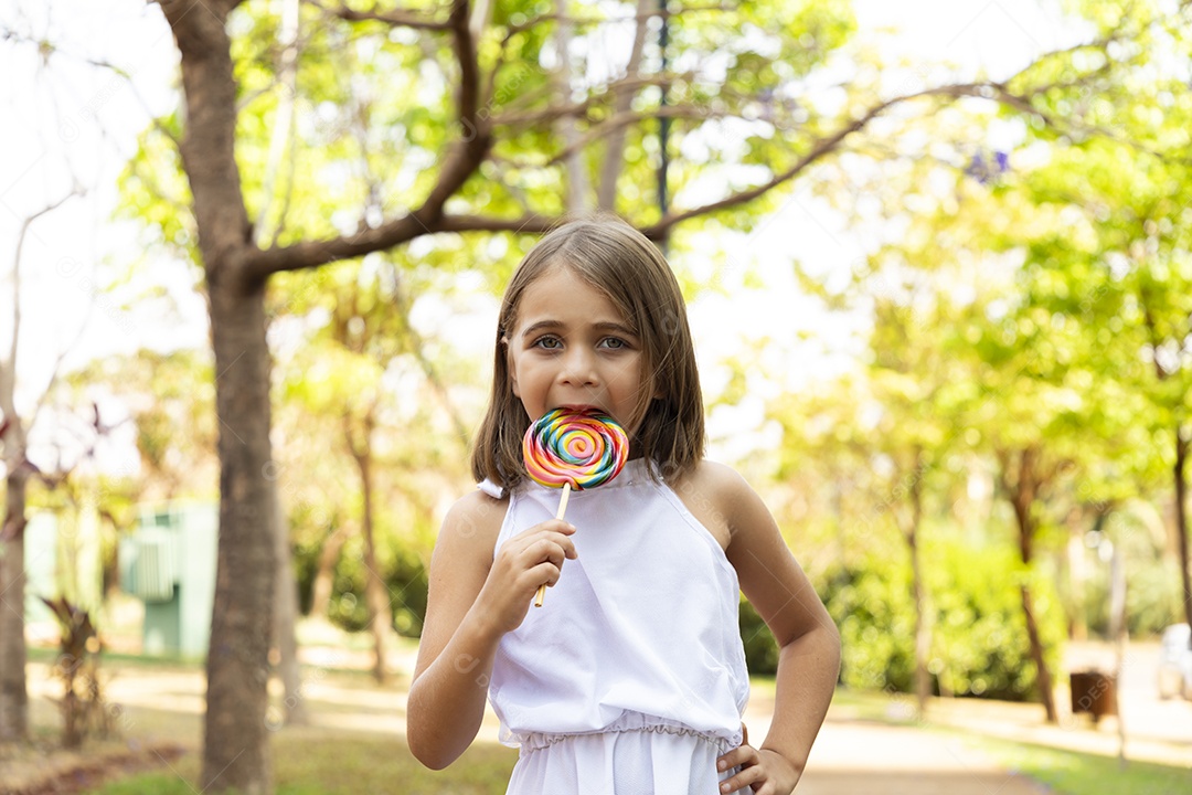 Menina loira chupando pirulito em um parque ao ar
