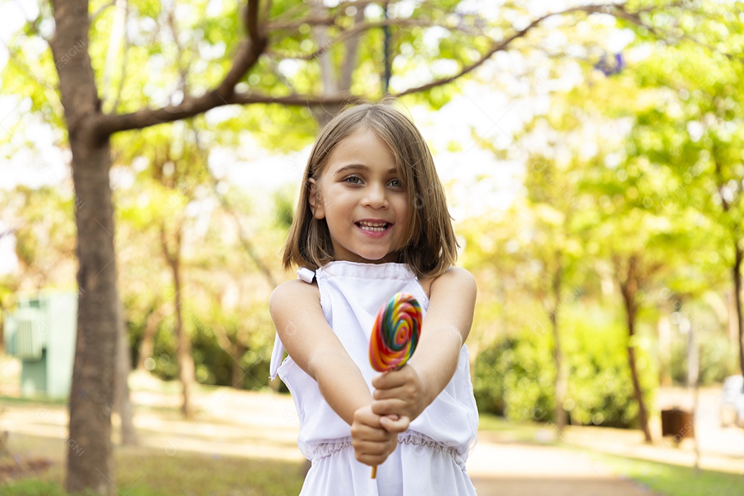 Menina fofa de vestido branco com seu pirulito nas mãos