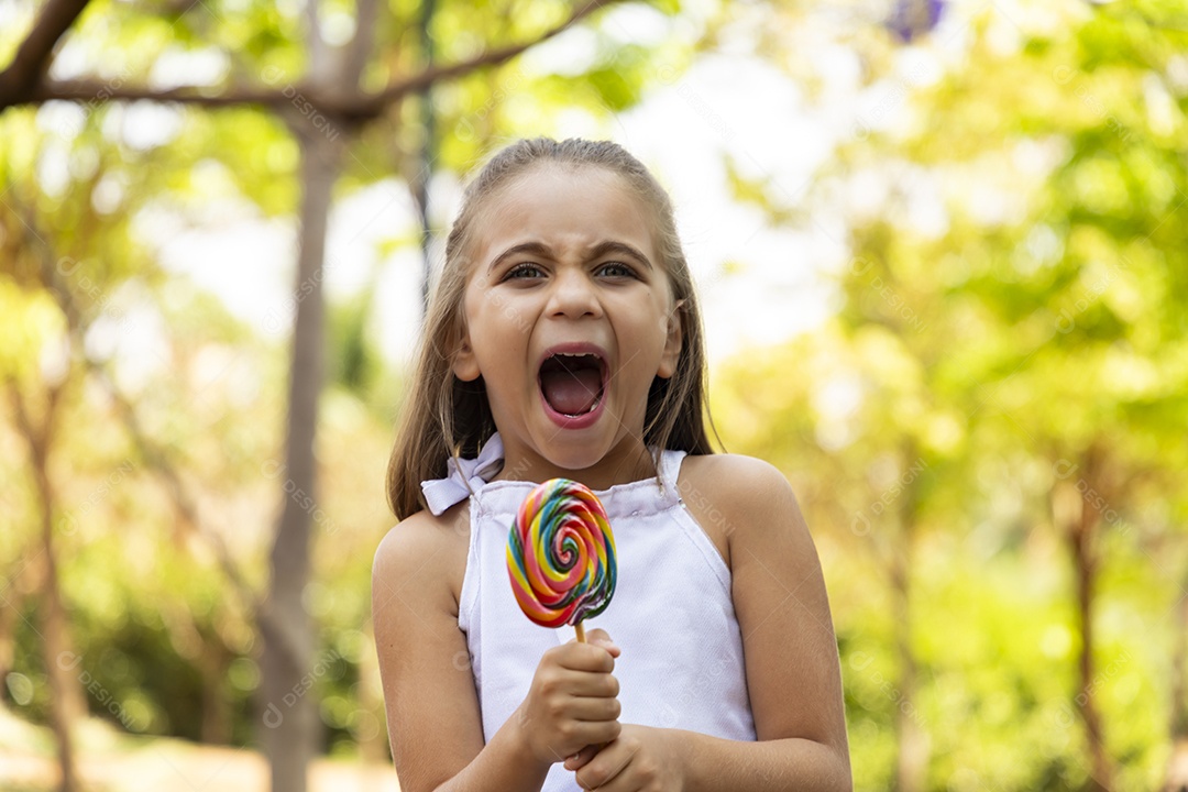 Menina feliz com seu pirulito na mão e boca aberta