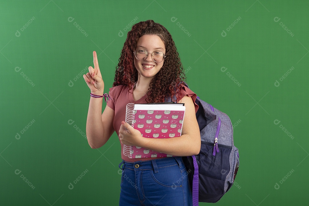 Menina apontando para cima segurando caderno e mochila nas costas