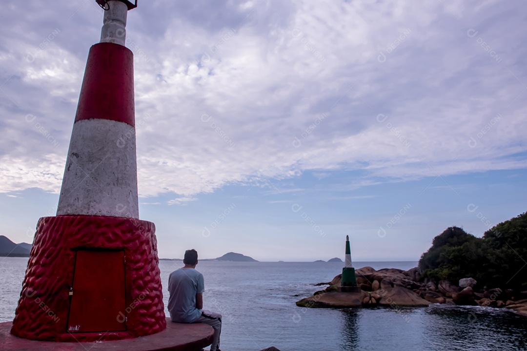 Homem sentado ao lado do farol observando o mar