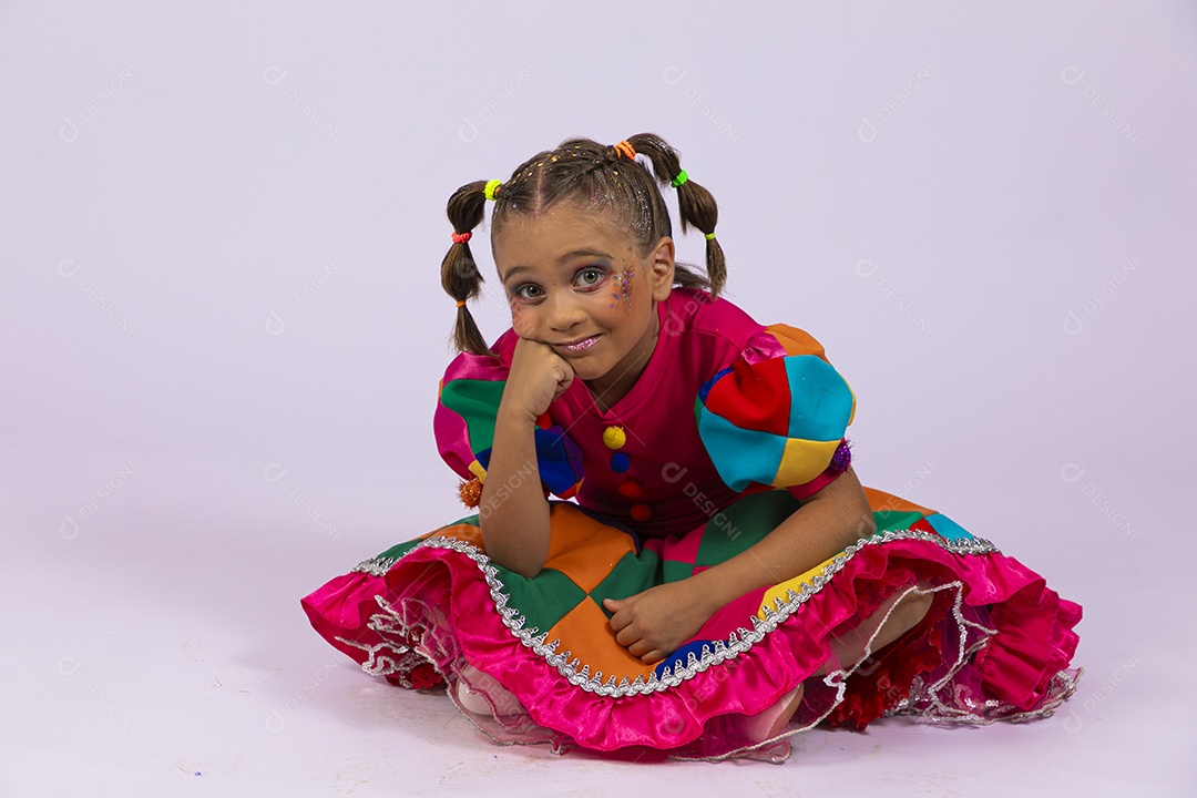 Menina fofa com roupa colorida sentada no chão com mãos no queixo