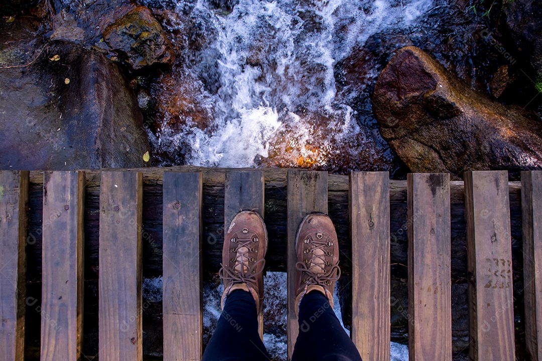 Vista dos pés no topo da ponte com o rio correndo por baixo