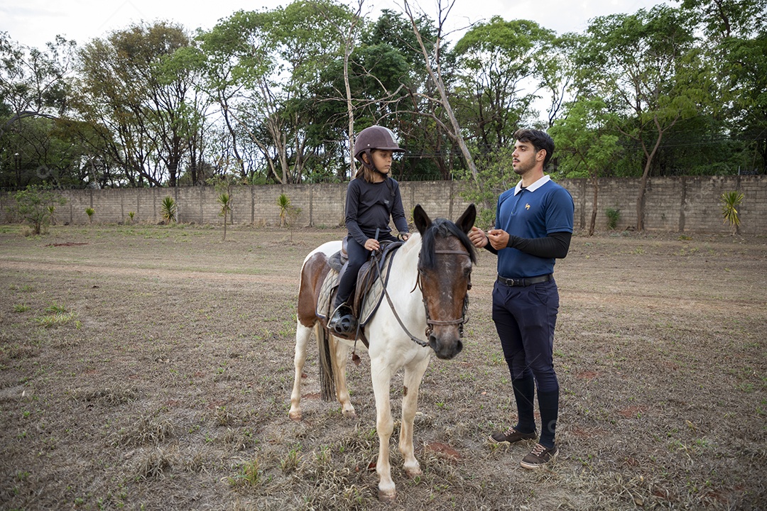 Garotinha em cima do cavalo com treinador ao lado