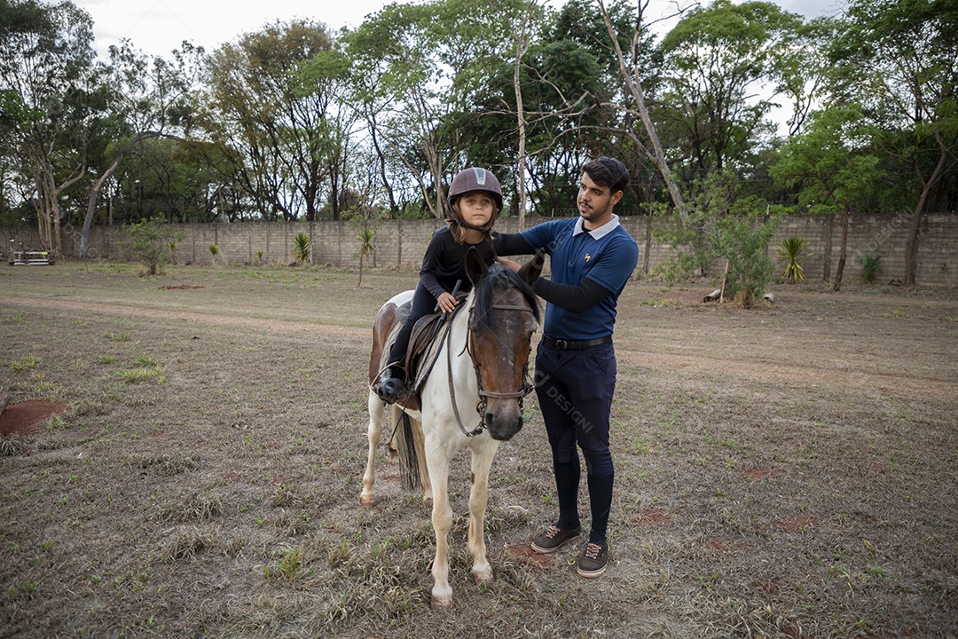 Garotinha em cima do cavalo com treinador ao lado