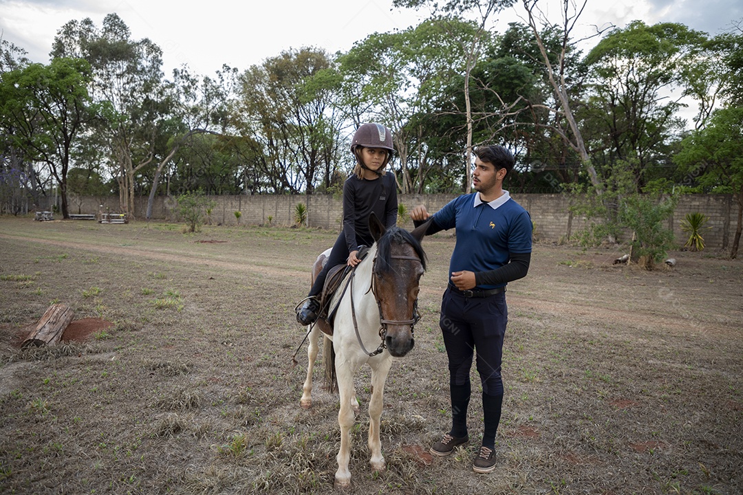 Garotinha em cima do cavalo com treinador ao lado