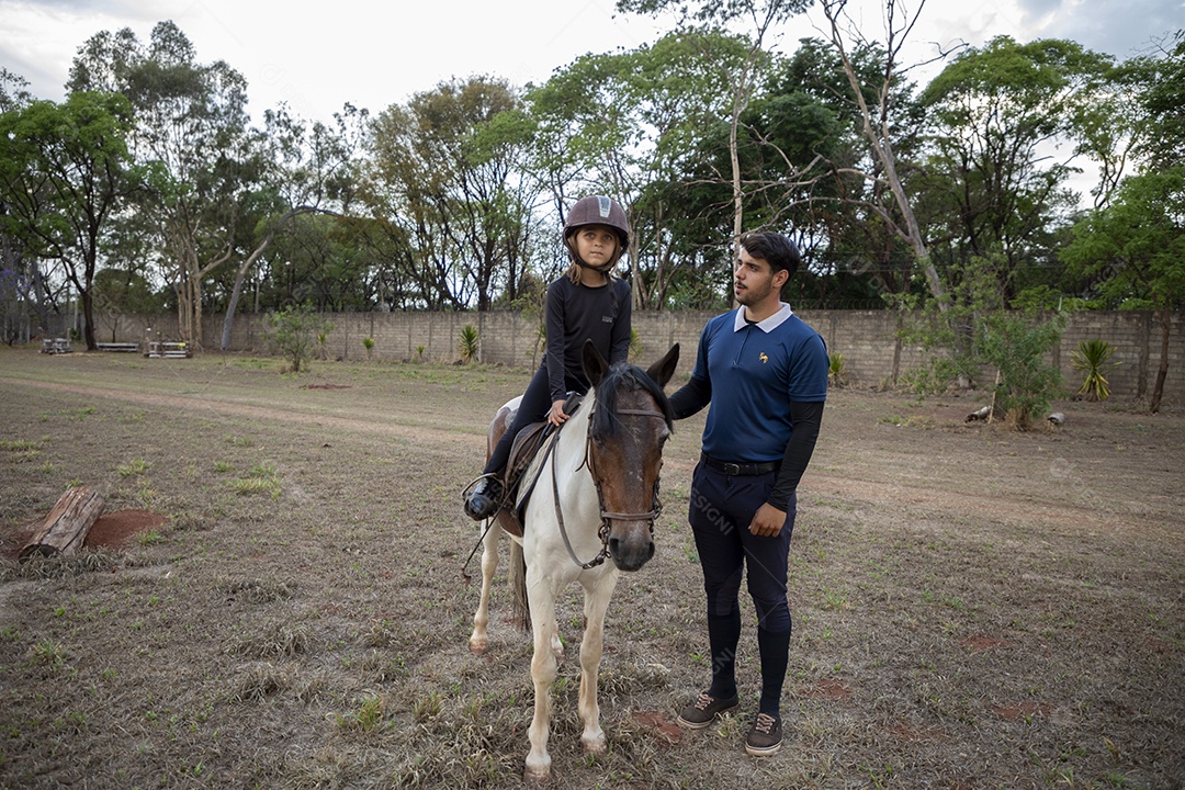 Amazona em cima do cavalo e treinador ao lado