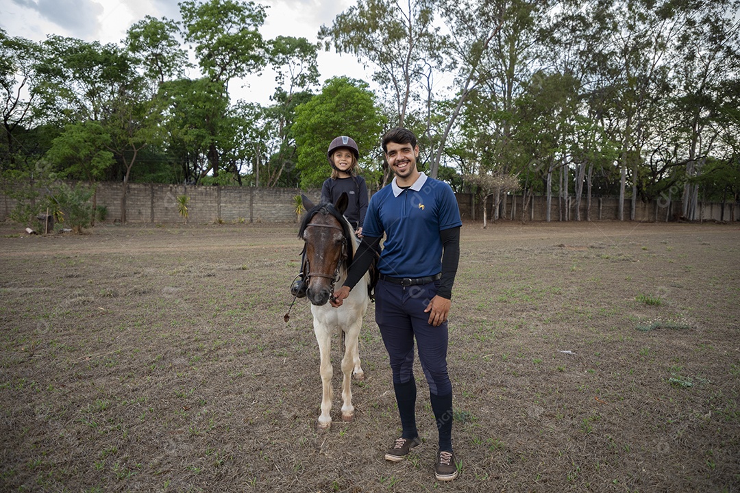 Treinador segurando na rédeas do cavalo com amazona para treino