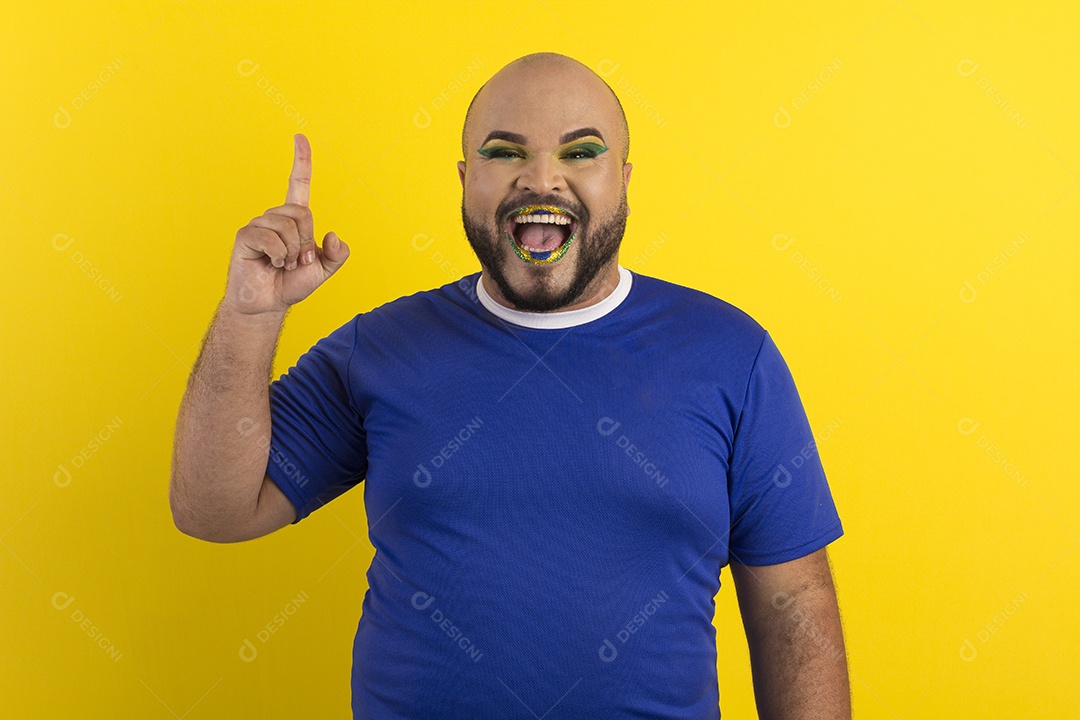 Um jovem gay feliz maquiado com camiseta azul apontando para cima