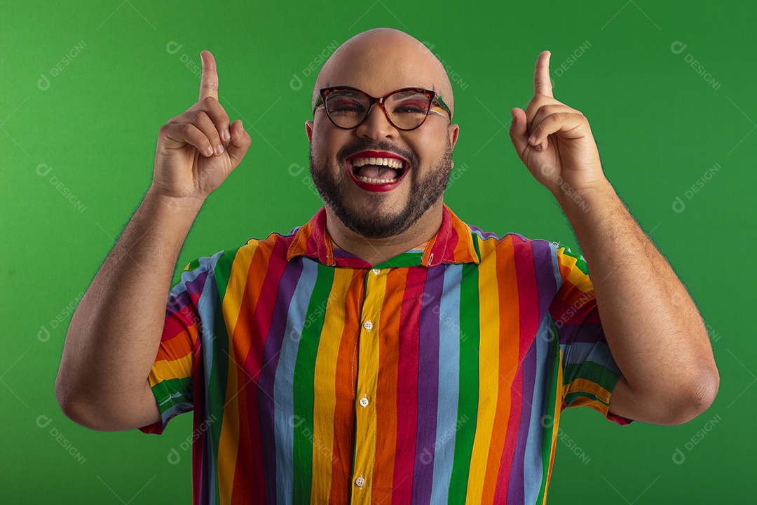 Jovem gay lindo usando camiseta e óculos colorido apontando para cima