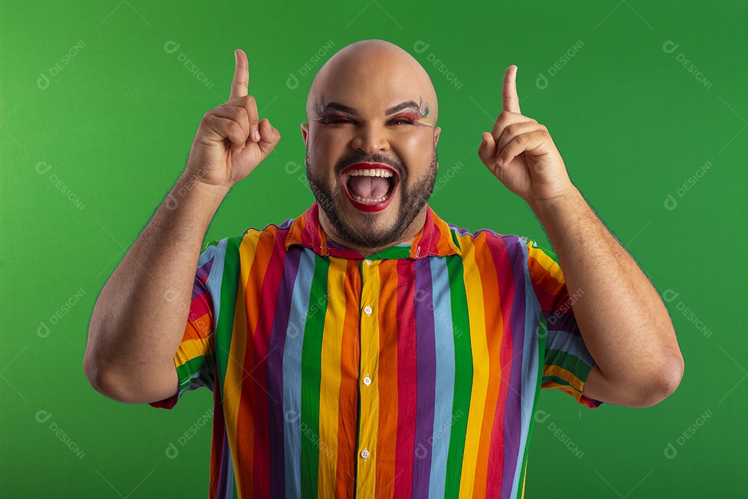 Homem gay com camiseta colorida e maquiado apontando para cima