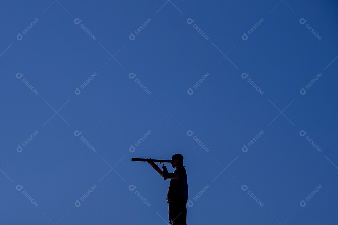 Silhueta de homem com luneta céu azul ao fundo