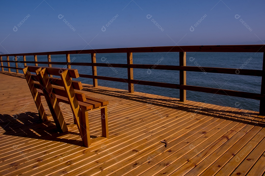 Banco de madeira em um deck com vista para o mar e o céu azul