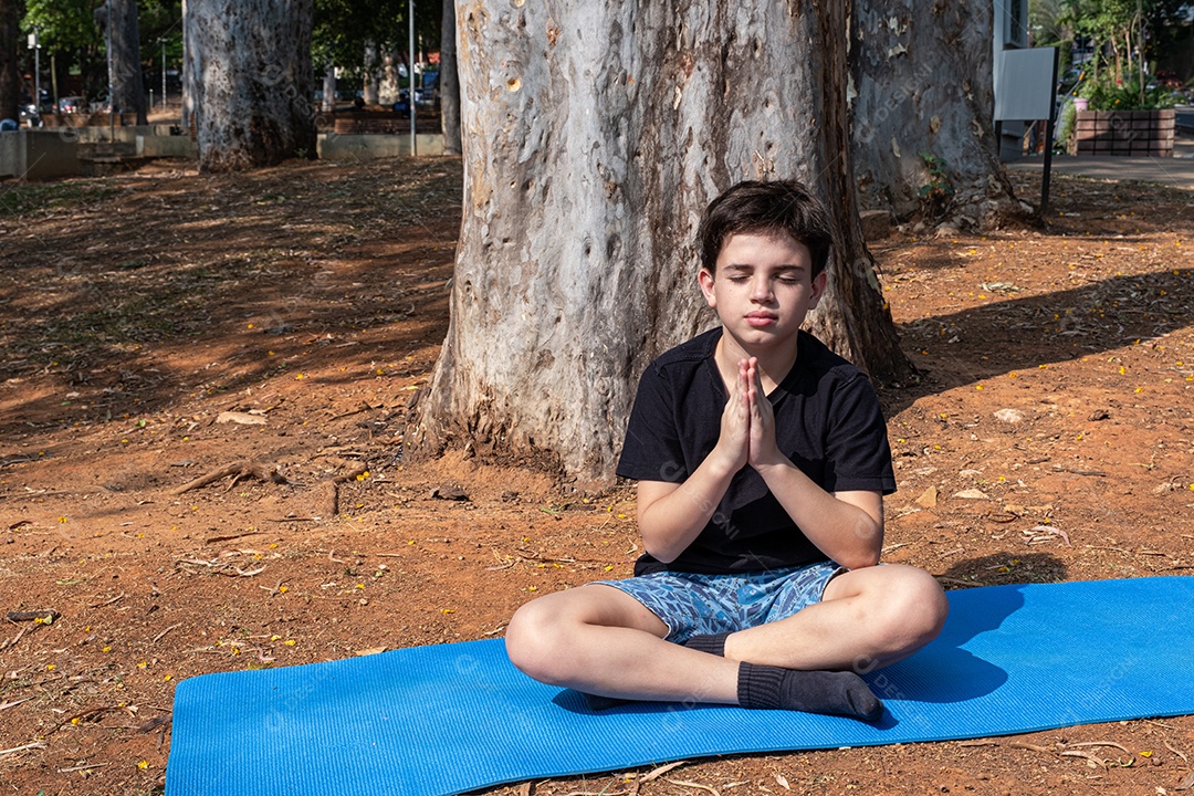 Menino sentado no tapete de yoga se alongando na aula ao ar livre