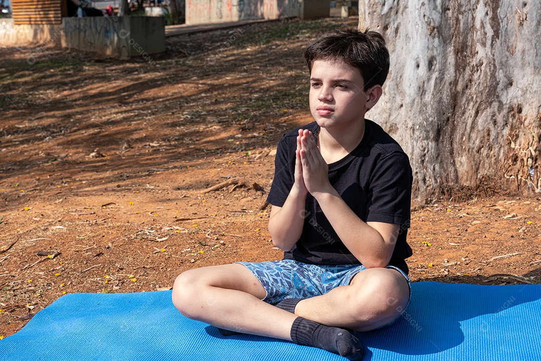 Menino sentado no tapete de yoga se alongando na aula ao ar livre